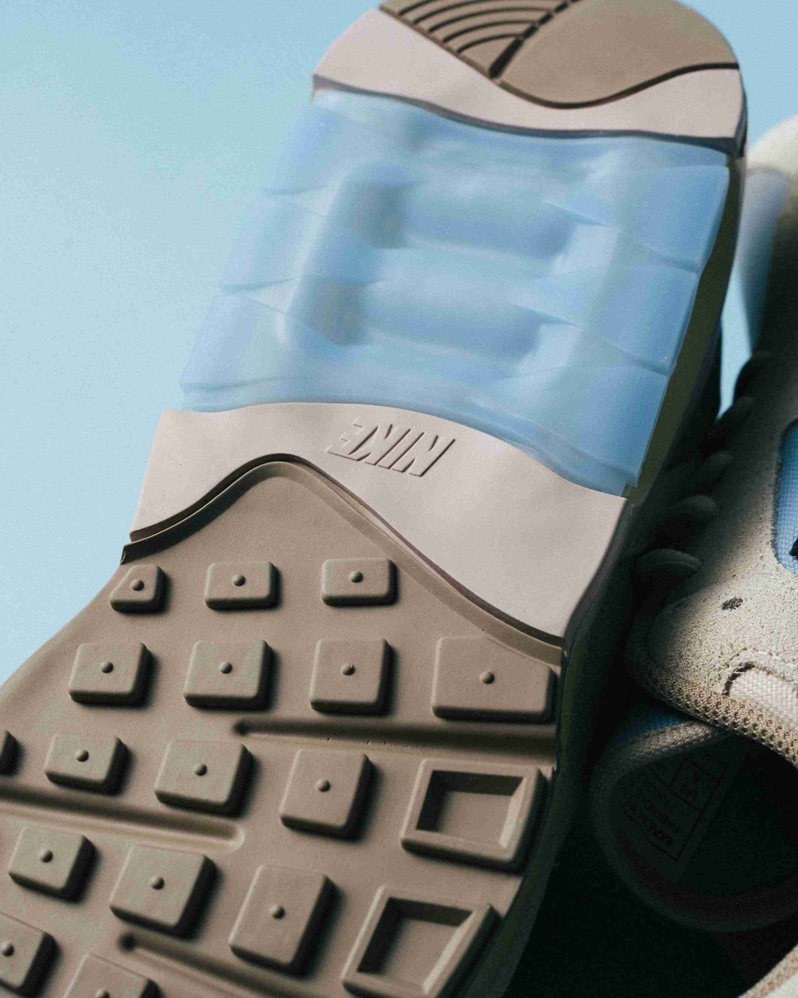 Paire de sneakers beige et bleu clair posée sur un fond bleu, vue de trois quarts avec mise en avant des formes et détails du modèle.